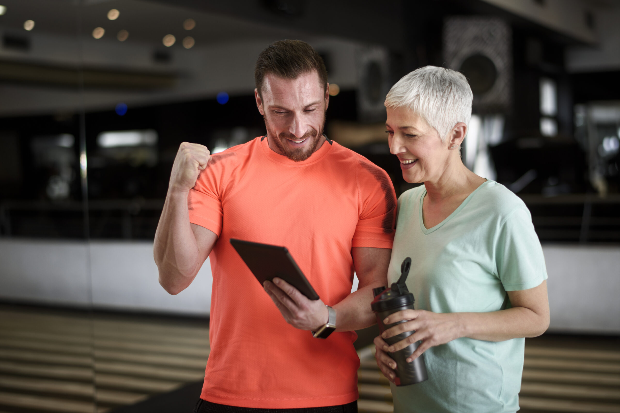 Active senior female in the health club being motivated by personal trainer with multimedia content on digital tablet.